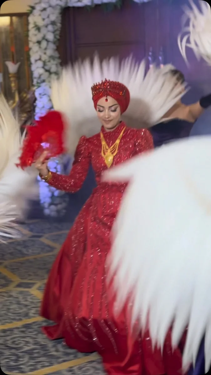 Beyaz tüy dekorları arasında kırmızı kına kıyafetiyle dans eden gelin